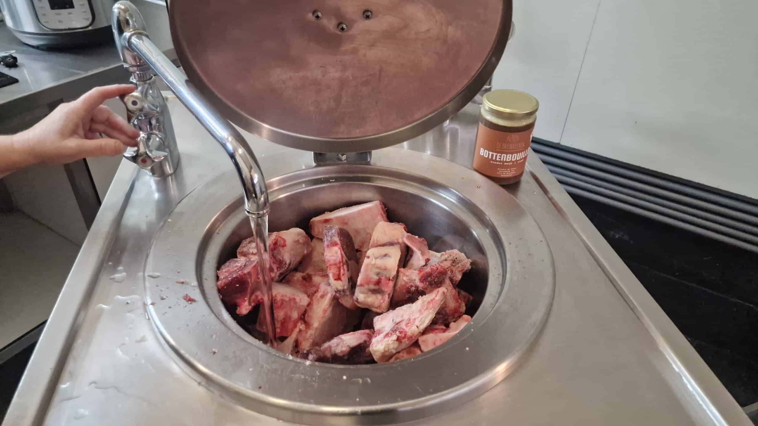 Rauwe runderbotten met bouillon in een roestvrijstalen pot.
